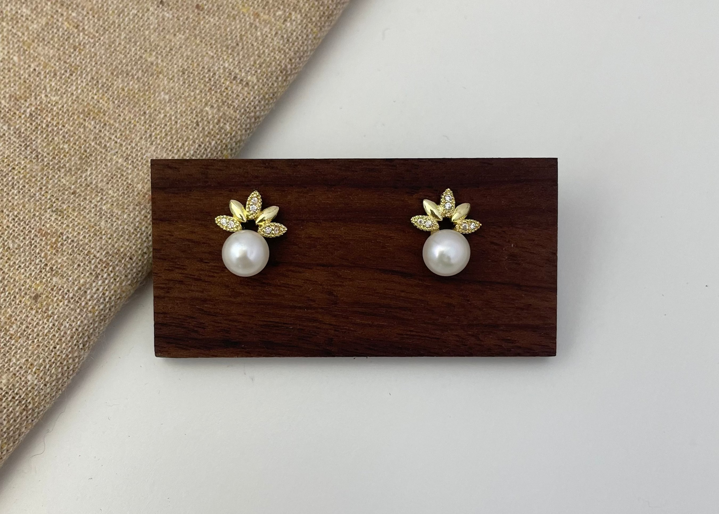 Pair of pearl earrings with gold leaves on a wooden display card against a neutral background
