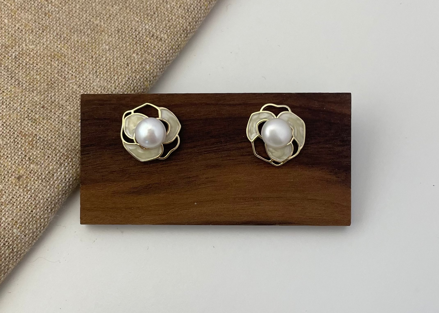 Pair of pearl earrings on a wooden display block with a beige fabric background