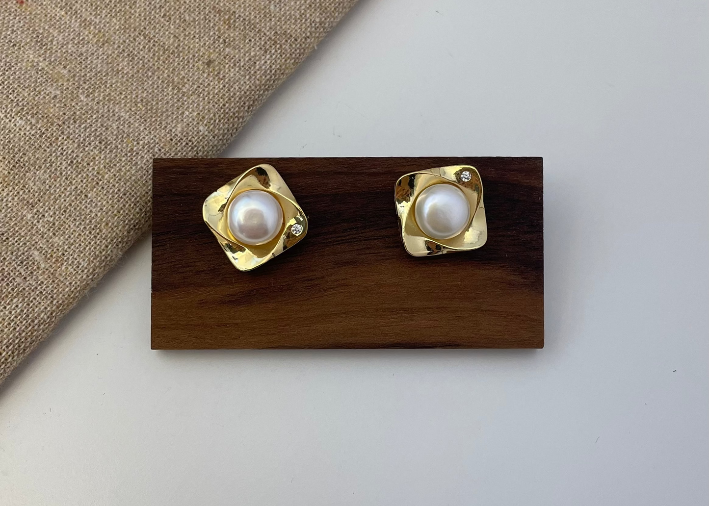 Pair of gold earrings with pearl centers on a wooden stand against a neutral background