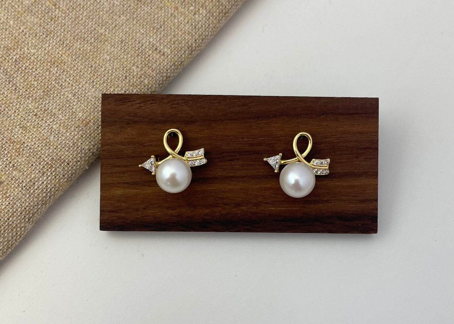 Pair of pearl earrings with gold accents on a wooden display block.