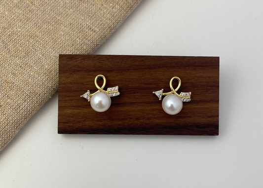 Pair of pearl earrings with gold accents on a wooden display block.