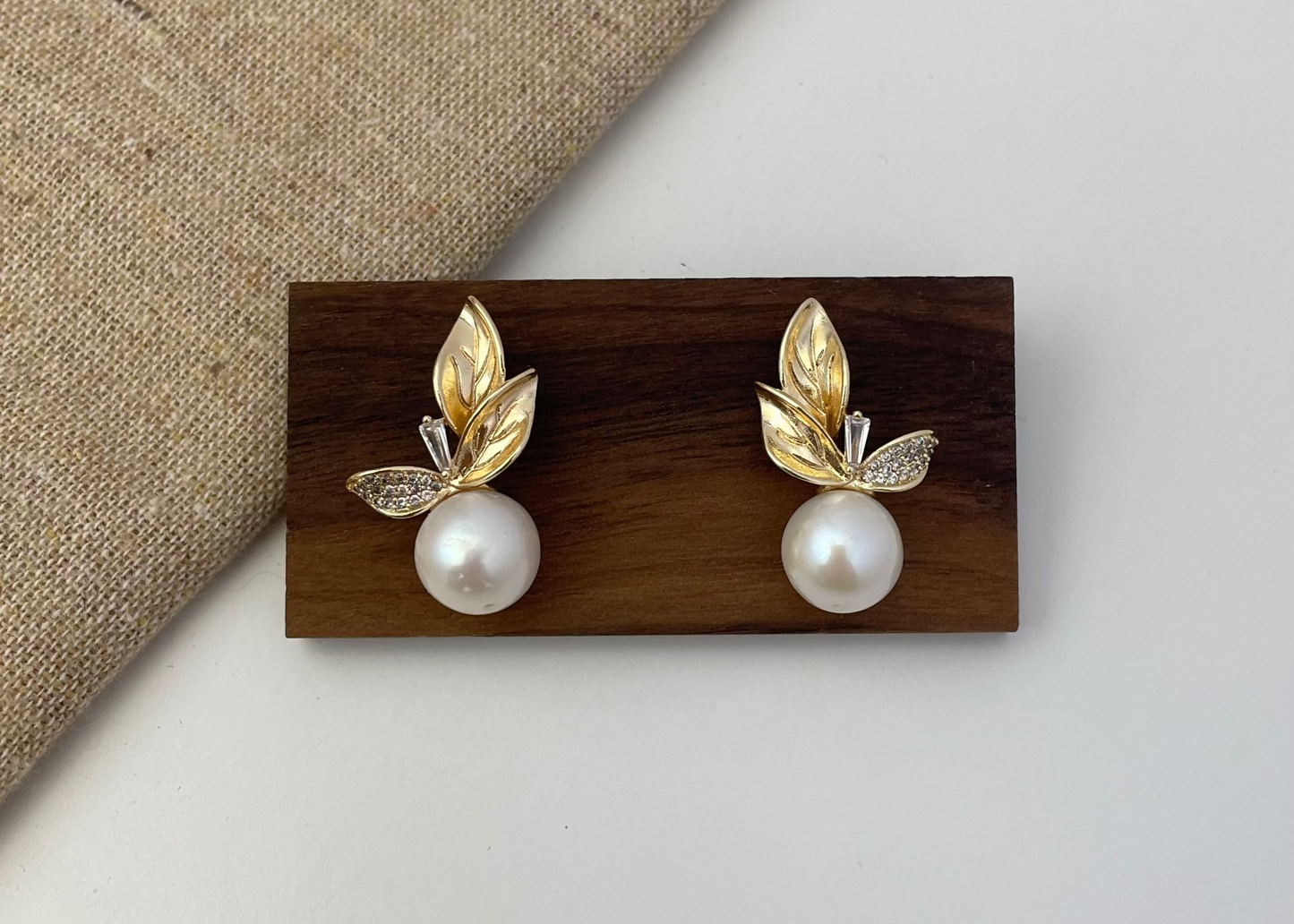 Pair of gold leaf earrings with pearls on a wooden stand against a neutral background